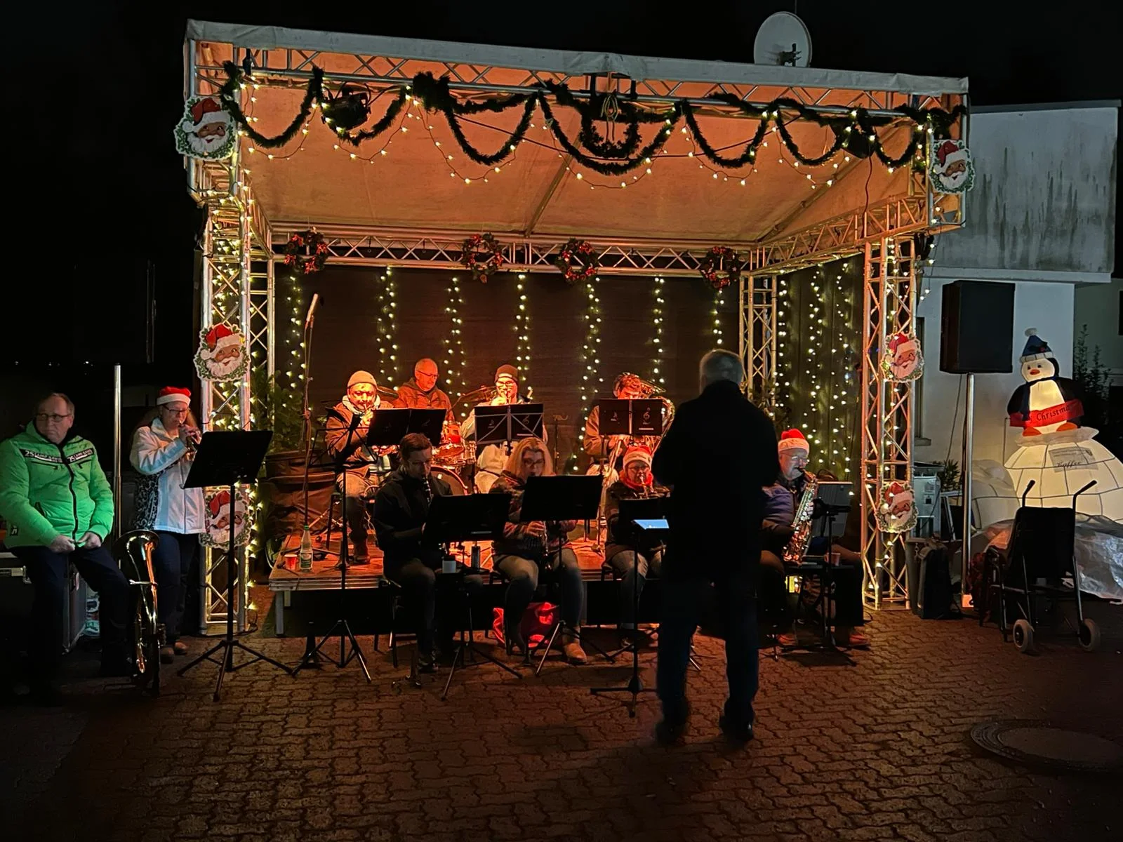 Musiker mit Blasinstrumenten auf einer mit Lichterketten geschmückten Weihnachtsbühne