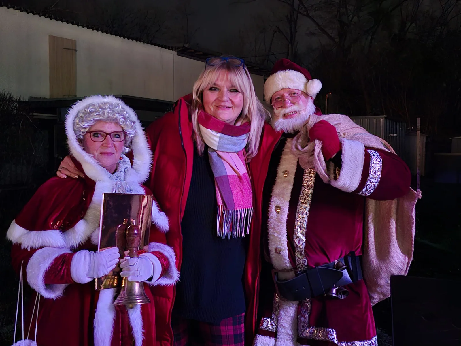 Drei Personen in festlichen Weihnachtskostümen bei einem früheren Weihnachtsmarkt